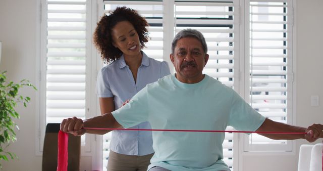 An African American female physical therapist guiding a senior man in a rehabilitation exercise using a resistance band. Ideal for content related to healthcare, physical therapy, elderly care, injury recovery, and professional healthcare services.