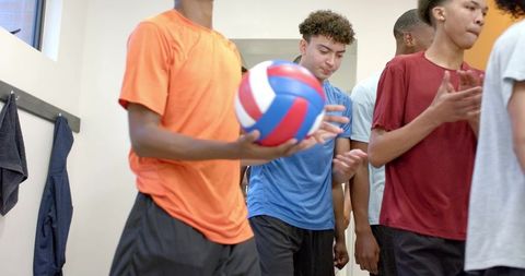 Male teen athletes walking hallway holding volleyball, team preparing for practice