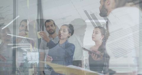 Business team collaborating on glass board, pointing at sticky notes and data analytics