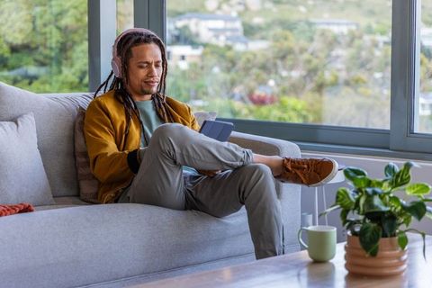 African american man relaxing on sofa with tablet and headphones in bright living room