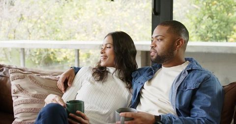 Couple Relaxing on Sofa Holding Mugs Enjoying Cozy Morning and Balcony Greenery