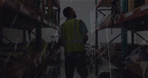 Warehouse worker checking inventory in low-light industrial aisle wearing hi-vis vest
