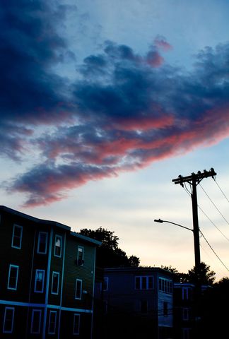 Dramatic pink and blue sunset clouds sweeping over silhouetted neighborhood buildings and utility po