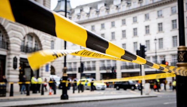 Yellow-black caution tape cordoning city street, police officers securing urban perimeter