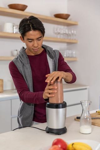 Young asian man preparing chocolate banana smoothie on modern minimalist kitchen counter