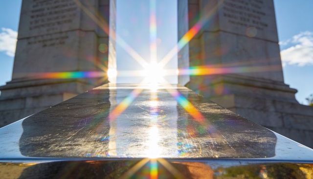 Sunstar bursting between stone pillars with polished handrail reflections and prism flares