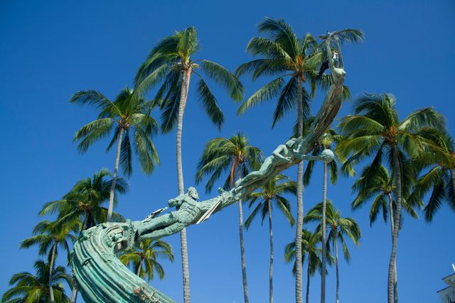 Statue against clear blue sky with palm trees in background. Perfect for representing tropical destinations, vacation spots, outdoor art installations, or serene natural settings.