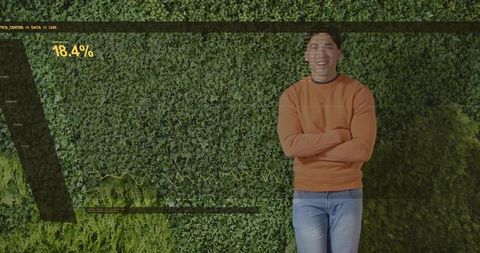 Standing man smiling in orange sweater against green living wall with 18.4% data overlay