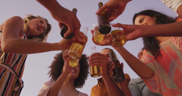 Happy diverse group of friends on beach, drinking a toast with beers and cocktails at sunset. Summer, free time, friendship, party, celebration and vacations.