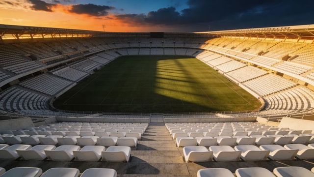 Empty modern stadium bathing in golden sunset light showing white seating and green pitch