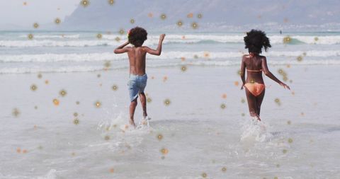 Children running and splashing in shallow surf on sunny beach with golden sparkles