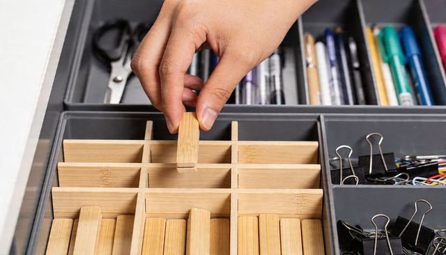 Hand arranging bamboo drawer organizer dividers in tidy home office supply drawer