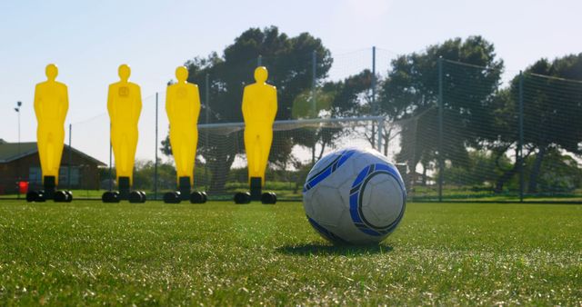 Soccer ball placed on a grassy field with yellow practice dummies in the background. Ideal for content related to sports training, coaching drills, or outdoor recreational activities.