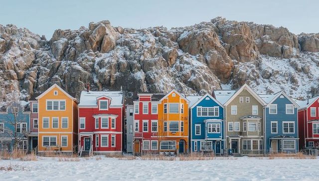Colorful wooden houses lining snowy foreshore at base of rugged rocky cliff