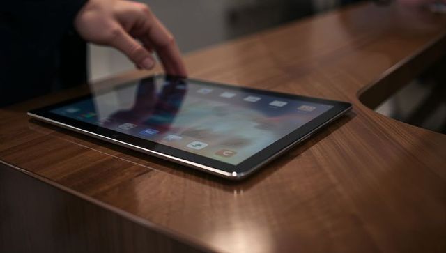 Hand Tapping Tablet on Polished Wood Counter in Tech Retail Showroom Display