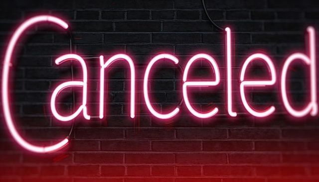 Canceled neon sign glowing pink against dark brick wall with red glow and exposed cable