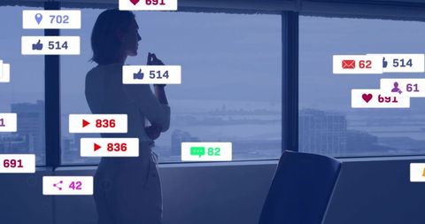 Businesswoman standing by office window gazing at city skyline with social icons overlay