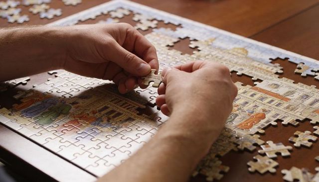 Hands Assembling Vintage Architectural Jigsaw Puzzle on Wooden Table Closeup with Pieces