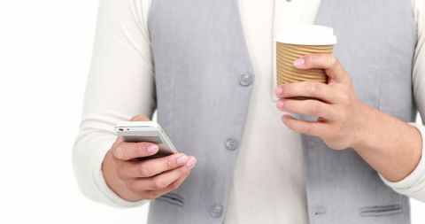 A young Caucasian woman holds a smartphone and coffee cup, showcasing a typical modern multitasking scenario. Perfect for illustrating concepts related to professional life, coffee culture, work breaks, or social media engagement. Useful in marketing campaigns focusing on lifestyle, tech gadgets, or productivity tools, where conveying balance and efficiency is crucial.