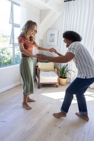 Couple holding hands and leaning playfully barefoot in sunlit minimalist loft living room