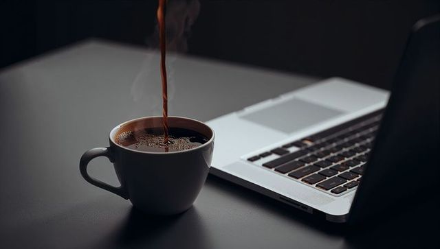 Pouring Fresh Coffee into White Mug Next to Laptop on Minimal Dark Workspace for Productivity