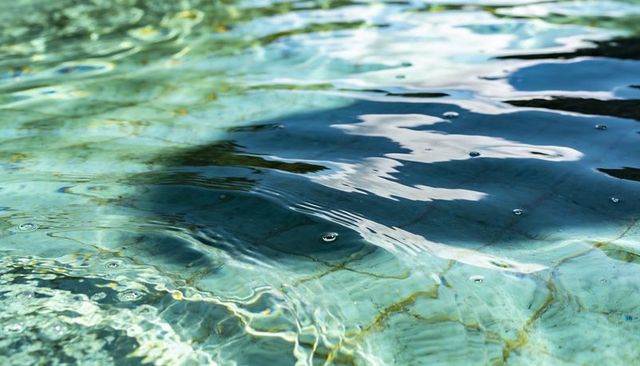 Turquoise pool rippling over mosaic tile bottom with sunlit caustics and small bubbles
