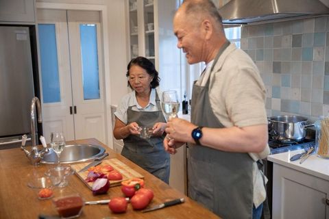 Asian couple cooking together in modern kitchen sipping wine while chopping tomatoes