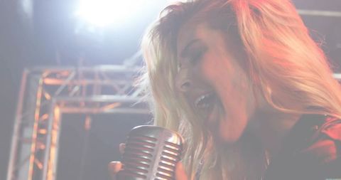 Blonde singer gripping vintage microphone singing under bright stage spotlight