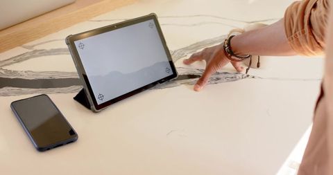 Tablet resting on folding stand on veined marble countertop with smartphone nearby