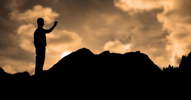Silhouette of a man standing triumphantly on a mountain during sunset, creating a dramatic and serene scene with warm hues in the sky. Ideal for concepts including victory, solitude, nature appreciation, and personal achievement. Perfect for travel, inspirational, and motivational content.