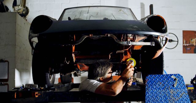 Caucasian man works on a car in a garage. He's focused on vehicle maintenance, showcasing skill in automotive repair.