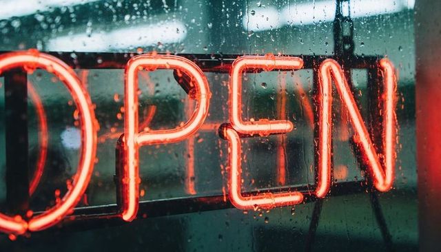 Neon open sign glowing through rainy shop window with red-orange reflections