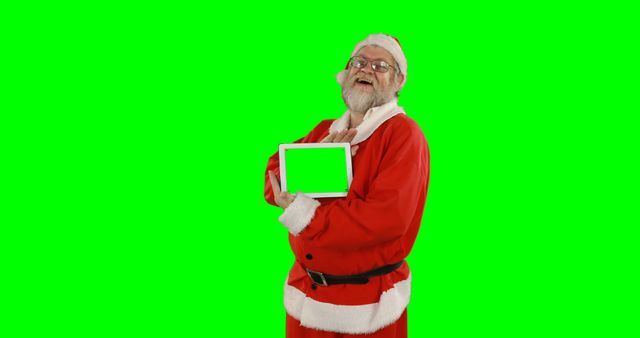 Santa Claus holding tablet on green screen setting for customizable holiday content. Ideal for digital campaigns, Christmas marketing promotions, festive themed projects, and any digital media usage requiring Santa Claus with versatile, green screen background for easy integration.