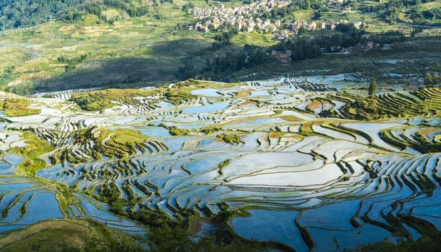 Sunlit terraced rice paddies reflecting sky across rolling hills mountain village panorama