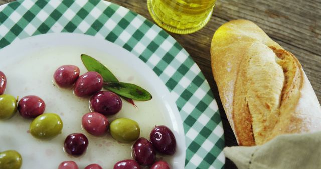 Colorful assortment of fresh olives accompanied by rustic bread and olive oil on a wooden table suggests Mediterranean-inspired cuisine. Ideal for food blogs, culinary magazines, farm-to-table dining promotions, and grocery store advertisements focusing on organic foods and healthy eating.