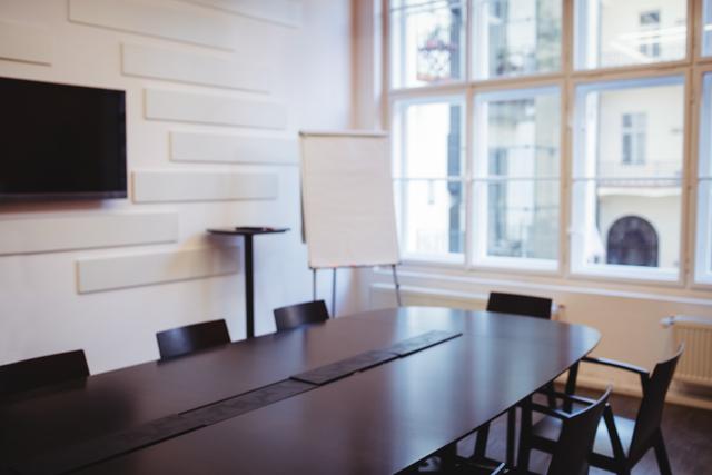 Modern business meeting room featuring a large conference table, chairs, and a presentation board. Ideal for illustrating corporate environments, professional meetings, and office settings. Suitable for business presentations, corporate websites, and office-related content.