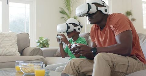 Father and son playing virtual reality games at home with VR headsets and controllers