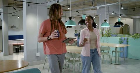 African American coworkers walking and talking in coworking space with tablet and coffee