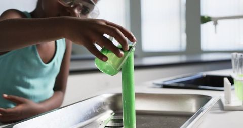 Young african girl pouring bright green science experiment liquid into sink