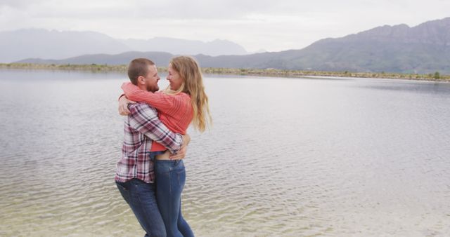 Couple hugging by a tranquil lakeside with mountains in the background. Suitable for romance, outdoor activities, travel, leisure, holiday promotions and lifestyle content.