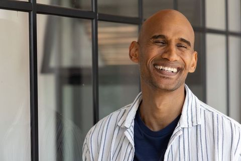 Smiling asian man leaning by glass grid in modern office striped shirt professional headshot