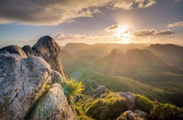 This image depicts a stunning sunrise over undulating mountains and rugged rock formations, bathed in golden sunlight and beneath a partly cloudy sky. Ideal for use in travel blogs, adventure magazines, nature-themed websites, and inspirational posters.