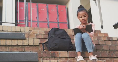 Student Studying on School Steps with Tablet and Backpack