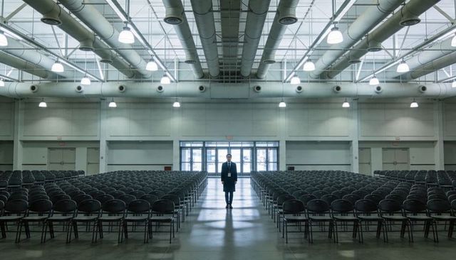 Event staff standing center aisle between rows of empty chairs in symmetrical expo hall