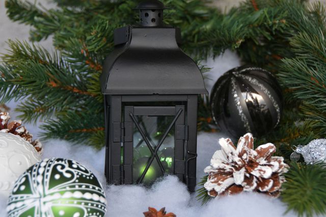 Black lantern surrounded by pine cones, green branches, and Christmas ornaments is creating a cozy holiday ambiance. Ideal for marketing holiday products, festive greeting cards, and decorating inspiration.