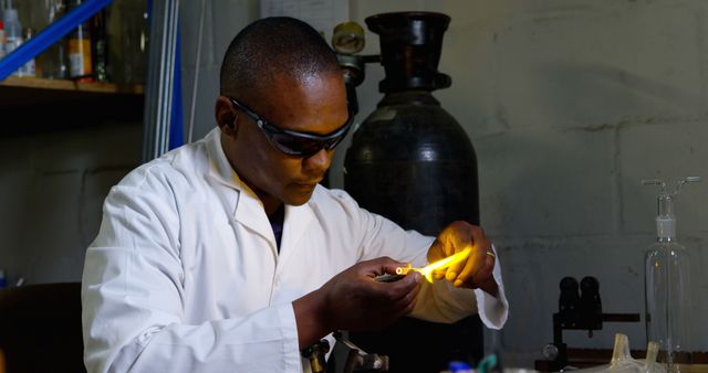 African American scientist conducting experiment in laboratory wearing safety glasses and lab coat. Suitable for themes related to scientific research, chemistry, laboratory work, and technology. Ideal for use in educational materials, scientific articles, promotional materials for research institutions, and visual presentations highlighting scientific processes.