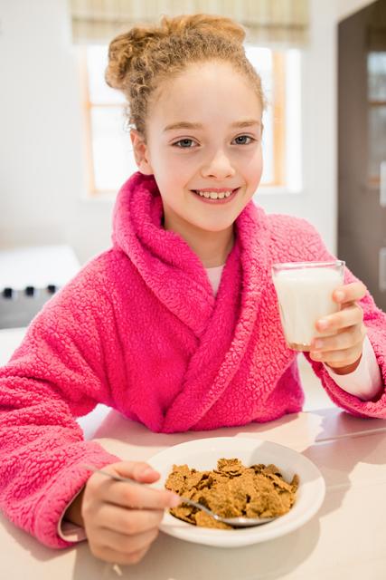 Cute girl in bathrobe having breakfast in kitchen at home