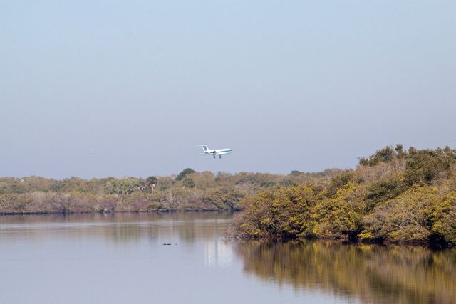 Image shows an airplane flying low over a calm river bordered by dense trees under a clear sky. Ideal for use in travel, tourism, aviation, or nature advertisements or blog posts.
