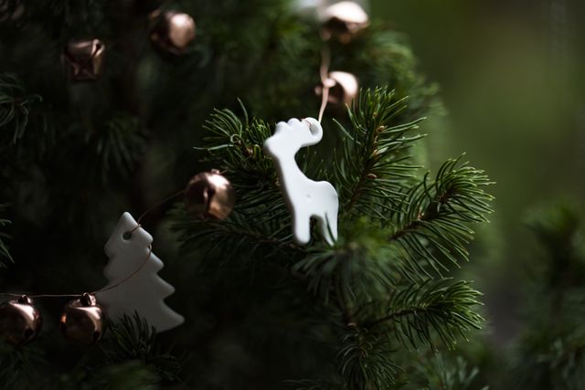This image shows close-up decorations on a Christmas tree, including a white reindeer ornament and small copper bells. Use this image for holiday-themed articles, festive blogs, Christmas cards, or seasonal marketing materials.