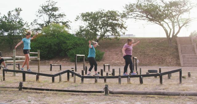 Group of women balancing on an outdoor obstacle course in a park. Ideal for depicting fitness, teamwork, and outdoor activities. Perfect for promoting exercise, summer activities, group challenges, and healthy living.